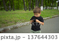 Child walking in park texting on phone during sunny summer day 4k 137644303