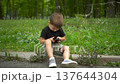 Little boy sitting on curb in park playing with smartphone summer 4k 137644304