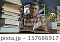 Man reading book surrounded by stacked library volumes indoors 137666917