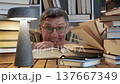 Man making funny faces while reading book among stacked volumes 137667349