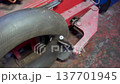 A tire is fixed to a machine in a workshop. Tools and equipment are visible around. It is a working area with some red and gray surfaces showing wear. 137701945