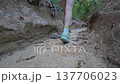 Close-up Low Angle Tracking Shot of a woman's legs and athletic shoe moving up a sandy path in a narrow ravine. Highlights motion and challenging terrain. 137706023