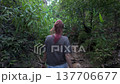 Close-up Back View of a woman with pink hair tips pushing through dense jungle plants. Focus on the challenging, overgrown nature environment. 137706677