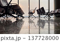 Airport seating area features modern chairs in rows, reflecting sunlight on the polished floor, creating a spacious terminal atmosphere with large windows 137728000