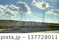 Wind turbines rotate in a green landscape with blue skies and clouds, highlighting the use of renewable energy in a rural environment 137728011