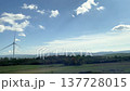 Wind turbines rotate in the breeze, set against a backdrop of green fields and hills under a bright blue sky, highlighting renewable energy sources 137728015