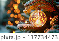 A stunning Christmas ornament hangs from a pine tree branch, illuminated by warm lights in a cozy winter atmosphere. Soft bokeh effects create a magical holiday feel. 137734473