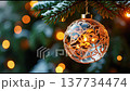 Beautiful Christmas ornaments dangle from a tree, glowing with warm lights. The atmosphere is joyful as the decorations bring holiday cheer into the room. 137734474