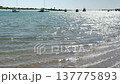 Bright sun creating shimmering reflections and sparkles on the tranquil ocean surface. With small waves gently lapping ashore and several boats anchored in the calm bay during a beautiful summer day 137775893
