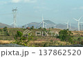 Wind turbines stand in a field along a road filmed from a moving vehicle while passing through a 137862520