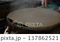 Thin rice batter spreads on a round steaming surface while cooking over heat in a kitchen area 137862521