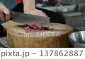 Vendor carefully slices thin pork pieces with a large knife on a wooden chopping block while 137862887