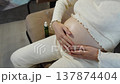 Pregnant woman applying oil to belly, closeup of glistening abdomen on couch with oil bottle nearby, gentle hands massaging skin, soft loungewear, cozy indoor prenatal selfcare and hydration routine 137874404