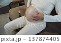 Relaxing pregnancy massage. Nurturing prenatal massage with soothing indoor lighting ambiance. Woman seated comfortably on sofa soothing her pregnancy with gentle oil massage and warm lighting 137874405