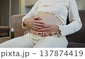 Woman's belly in seventh month of pregnancy. Woman in late pregnancy sits on couch, stroking her belly with hands, massaging baby in womb. Care and gentle stroking of belly. Stretch mark prevention. 137874419