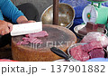 Market vendor carefully slices meat with a large knife on a wooden chopping block while preparing 137901882