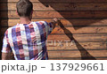 A man paints a wooden house with a brush. A man covers the wall of a wooden house  137929661