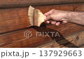 A man paints the wall of a wooden house with protective oil using a brush. A man paints a house.  137929663