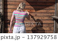 A woman paints a wooden house with a brush. A man covers the wall of a wooden house with oil. 137929758