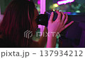 Excited woman looking on night city cityscape in binoculars telescope on observation deck for tourists. Colorful night lights view from top floor. Neon light, bokeh in background. Travel, tourism 137934212