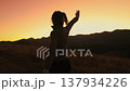 Woman dancing outdoor evening mountain sunset sky. Slim young girl silhouette having fun, moving, raise hands up, listening music in mountain hill, orange sunrise in background. Back view. Slow motion 137934226