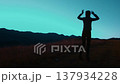 A tourist woman enjoys the serene landscape of the Carpathian Mountains at dusk, joyfully gesturing towards the horizon as the sky transitions to twilight. 137934228