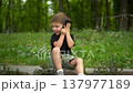 Three year old boy sitting on curb in park talking on phone 4k 137977189