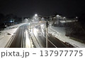 Winter, snow is falling. Lanterns on poles shine on the winter road. Cars and yellow bus drive on the slippery road  137977775
