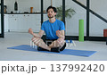 Calm handsome fit man in sportswear practicing relaxation exercise, sitting in lotus yoga pose on exercise mat while taking a break from indoor workout. 137992420