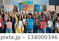 Multiracial students rally in city center holding colorful placards and chanting, urban skyline backdrop, enthusiastic young leaders raising fists, diverse crowd energy, daytime civic action 138000346