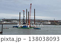 Two tugboats pushing and pulling a large jack up rig, a specialized construction barge with tall spud legs and a crane, maneuvering it for positioning in the harbor for marine engineering work 138038093