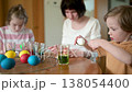 Two big sisters and their little brother dyeing Easter eggs at home. Slow motion 138054400