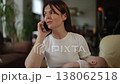 Stressed freelancer mother holding her newborn baby while calling on a smartphone 138062518