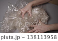 Frustrated person aggressively crumpling plastic wrap on gray table, showcasing stress, anxiety, environmental impact of single use plastic waste and pollution, close-up, slow motion. 138113958
