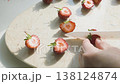 Hand cutting fresh strawberries with white ceramic knife on marble board. Halved organic red berries prepared for healthy snack or dessert in bright natural sunlight. 138124874
