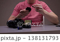 Professional content creator sitting at desk and attaching wireless lavalier microphone with furry windscreen to t-shirt, preparing equipment for video recording session in dark studio, close-up. 138131793