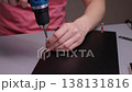 Person assembling furniture using electric screwdriver, fastening screws into black wooden panel, demonstrating do-it-yourself home improvement project with focused manual labor, closeup, slow motion. 138131816