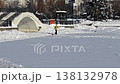 Middle-aged woman with fair skin in a yellow jacket cross-country skis on a snowy field near an arch bridge in a winter city park. 138132978