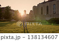 Relaxed female figure dances under warm sunset glow, Casual woman with long hair enjoys lively dance amid historic campus scenery 138134607