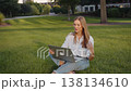 A young student working while sitting on the grass with a laptop. 138134610