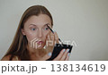 A woman while using eyebrow pencil for apply color to her eyebrows. Self makeup process 138134619