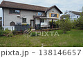 Two story house with overgrown lawn and small garden 138146657