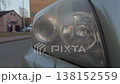 Aged foggy lens. Closeup captures hazy headlight surface reflecting soft urban storefront lights and signs 138152559