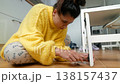 Woman Searches Floor. Young Woman On Tiled Floor Carefully Seeking Tiny Missing Item Near Furniture Leg 138157437