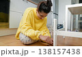 Woman Searches Floor. Young Woman On Tiled Floor Carefully Seeking Tiny Missing Item Near Furniture Leg 138157438