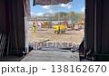 View from an unfinished building showing a construction worker in high visibility clothing walking across a busy construction site with heavy machinery like excavators and a soil compactor 138162670