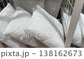 Numerous clean, white, and fluffy pillows neatly arranged in a large wire basket for sale in a retail home goods store, showcasing a wide selection of bedding and cushions for comfort 138162673