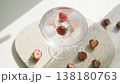Iced strawberry water in crystal glass on beige marble tray. Strawberries fall into glass. Halved organic berries and frozen ice cubes in refreshing summer drink with bright sunlight shadows. 138180763