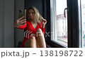 Gorgeous Blonde Woman in Red Dress Posing For Smartphone Selfie Camera by Window 138198722