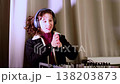 Young girl in casual jacket works carefully at a mixing console with headphones on, creating modern electronic music and developing creative technical skills. 138203873